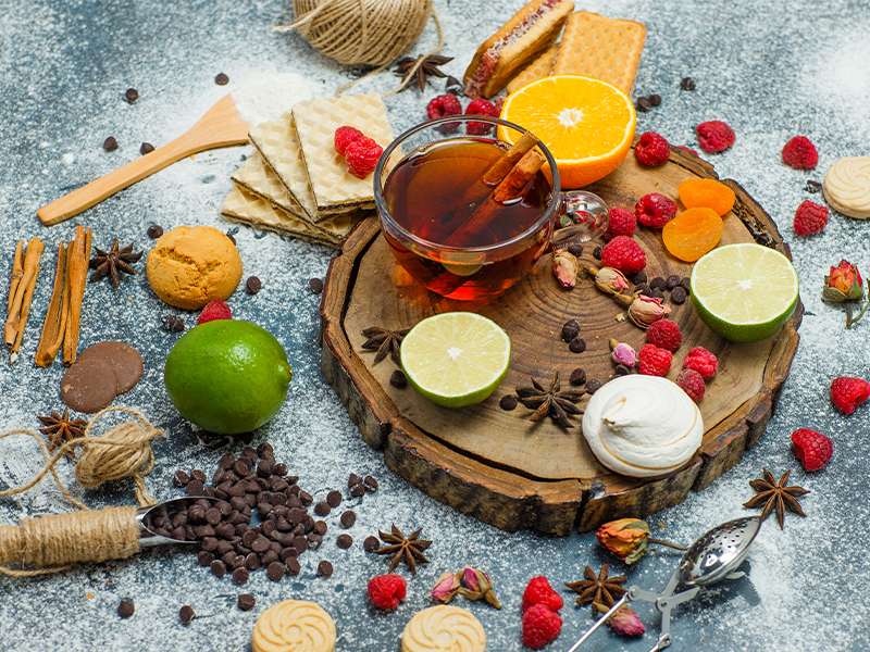 valerian root dried in bowl, steaming dandelion tea in glass cup, chamomile flowers next to tea, fresh peppermint leaves near teacup, red hibiscus tea on wooden table